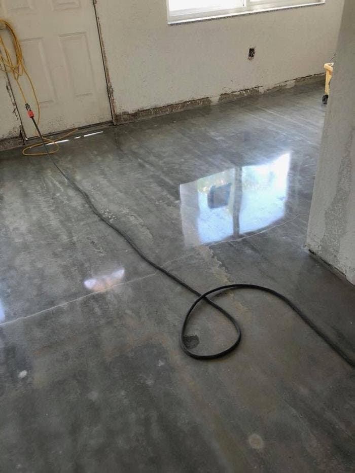 Ground and polished gray concrete floor in progress in a room with unfinished walls